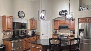 Una cocina moderna con armarios de madera, electrodomésticos de acero inoxidable, una isla central con sillas y un reloj en la pared.