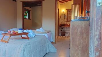 Quarto de hotel com duas camas, uma mesinha de madeira com itens de café da manhã, banheiro com pia e espelho, e vista para o exterior.