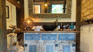 Un baño rústico con un armario azul antiguo, un espejo grande y un cuenco decorativo en la encimera.
