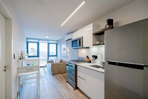 A modern kitchen with a stainless steel refrigerator, a microwave, and a stove. There is a window providing a view of the city.