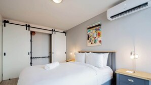 Una habitación de hotel con cama, mesita de noche, aire acondicionado de pared y una obra de arte en la pared.