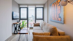 Un salón moderno con sofá, una mesita, una planta y un ventanal con vistas a la ciudad.