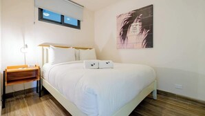 Ein Schlafzimmer mit Bett, Nachttisch, Wandbild und Fenster.