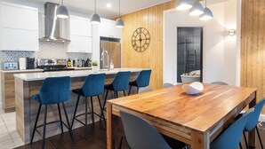 A modern kitchen with a central island, bar stools, pendant lighting, and a wooden wall clock. - Le Saphir, NEW, Spacious 2-bedroom Condo, Downtown Quebec City 5*, Quebec City (Québec)