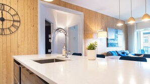 A modern kitchen with a large island, built-in dishwasher, and a wall-mounted clock. - Le Saphir, NEW, Spacious 2-bedroom Condo, Downtown Quebec City 5*, Quebec City (Québec)