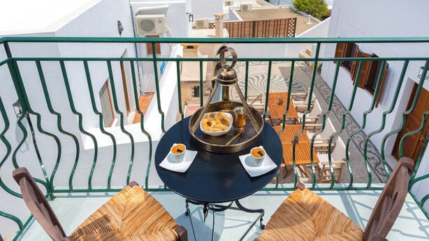 Un balcon avec deux fauteuils en osier, une petite table agrémentée d’un objet décoratif, et une vue sur la ville et la mer.