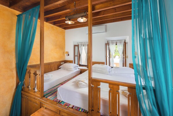 Una habitación con dos camas de madera, cortinas color turquesa y techo de madera.