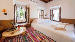 Une chambre d’hôtel avec deux lits, un plafond en bois, une moquette rayée aux couleurs vives et une petite table avec une lampe et une bouteille.