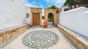 Une cour avec un sol à motifs, un grand pot en terre cuite et une arche en pierre menant à une porte en bois.