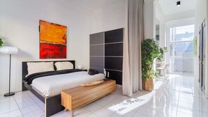 Un dormitorio moderno con una cama grande, un banco de madera, una planta en maceta y vistas al exterior.