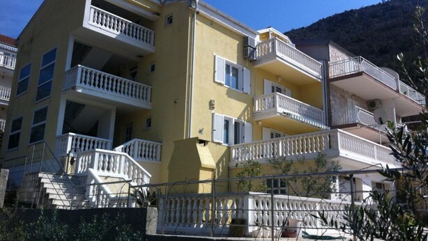 A multi-story building with balconies, a stairway leading to the entrance, and a mountainous backdrop.