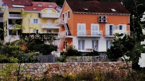 A row of colorful houses with balconies, a stone wall in the foreground, and lush greenery.