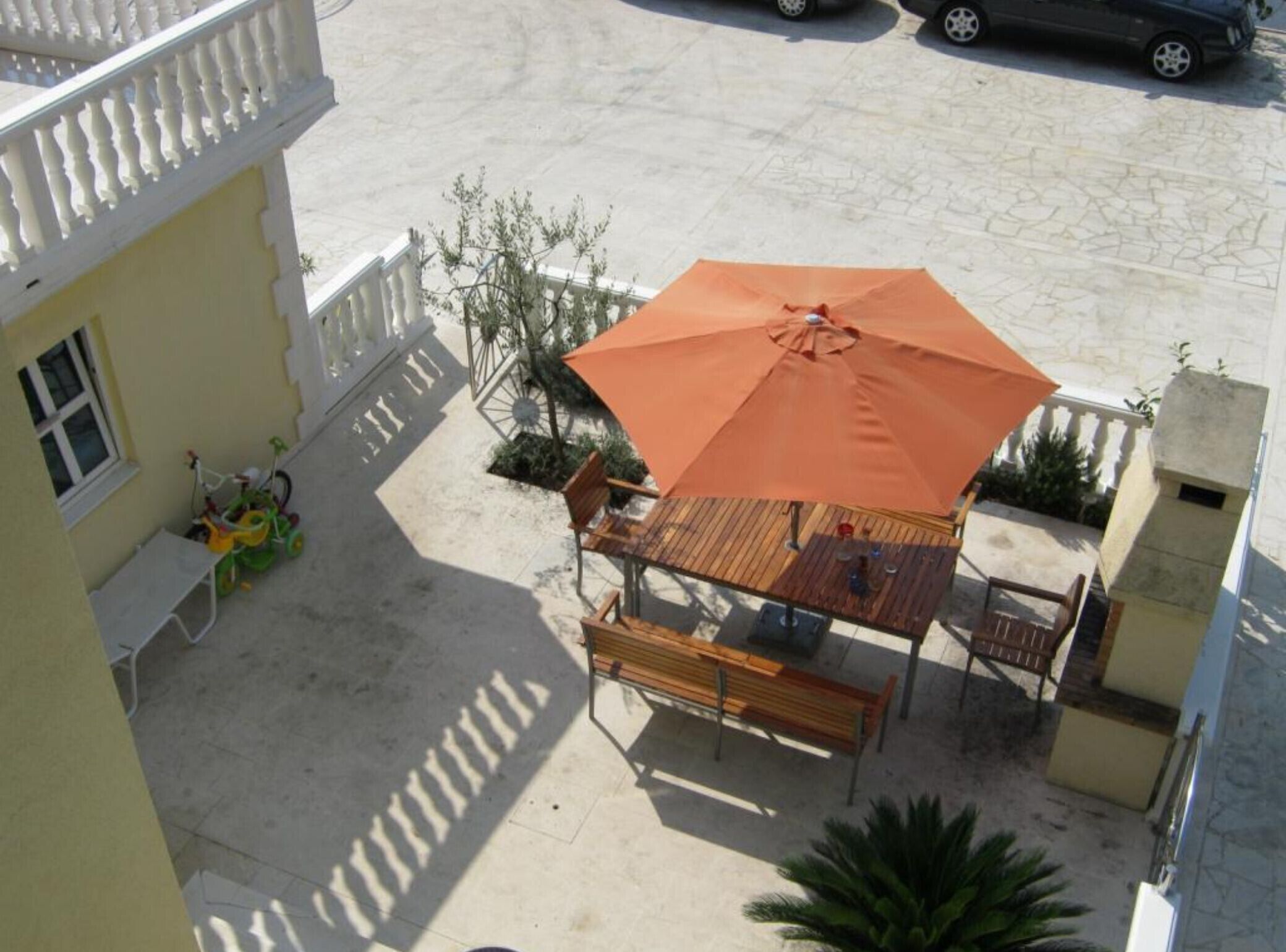 Un patio con una mesa y sillas de madera, una sombrilla naranja y una bicicleta.