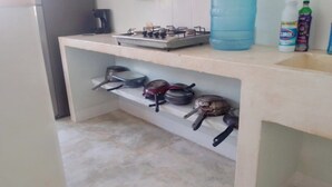 Een keuken met een gasfornuis, een koffiezetapparaat en verschillende pannen en braadpannen op planken.
