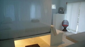 Een kamer met een bed, een stoel, een kleine tafel en een ventilator.