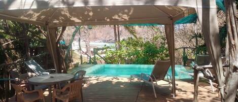 A covered outdoor area with a pool, lounge chairs, and a table.