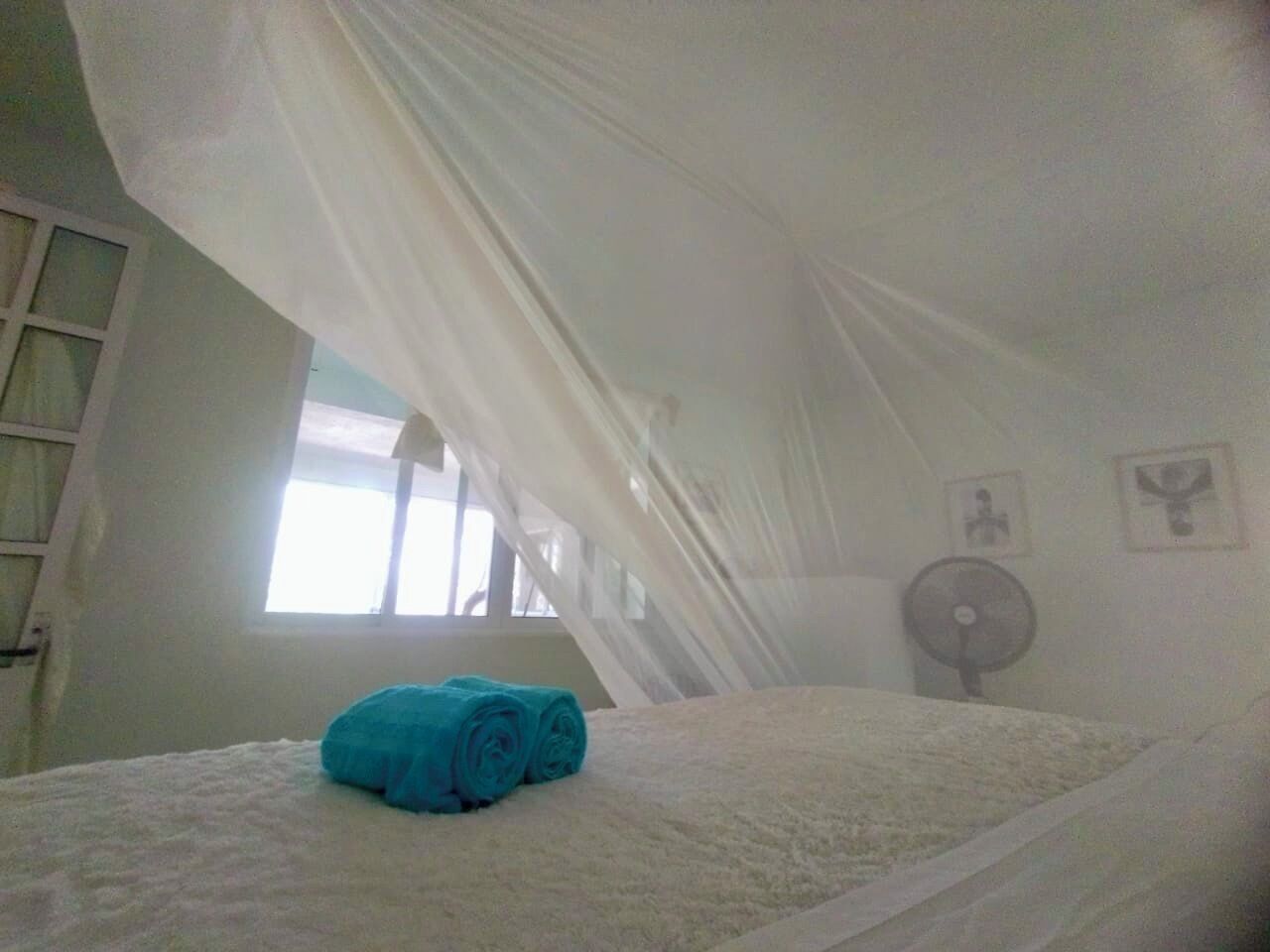 Une chambre à coucher avec un lit, une fenêtre, un ventilateur et un mur orné de deux tableaux encadrés.