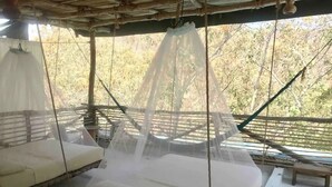 Een kamer met een bed onder een klamboe, een bankje en uitzicht op bomen.