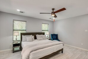 Un dormitorio con cama, mesitas de noche, una silla y un ventilador de techo.