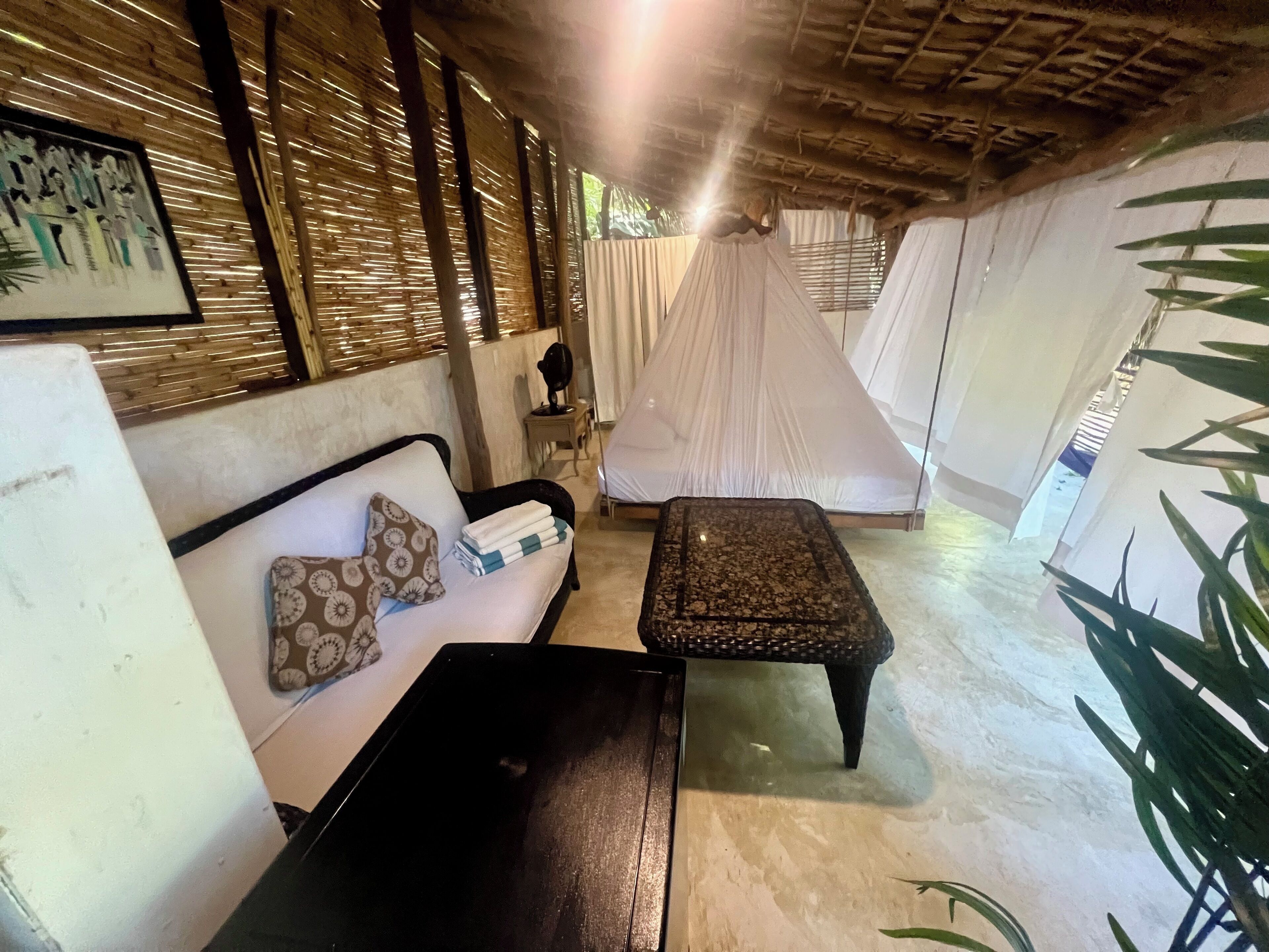 A room with a wooden ceiling, a sofa with patterned cushions, a small table, and a canopy bed.