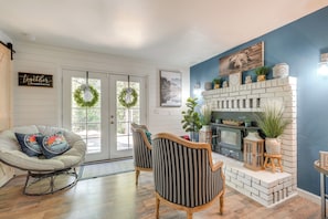 Cozy living room with a fireplace, two chairs, and a sofa, featuring a brick fireplace and wooden floor.