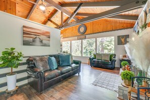 Relax in this spacious living area with a high ceiling and large window, featuring a sofa, smaller sofa, and decorative items.