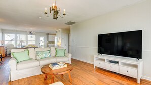 A living room with a white sofa, a coffee table, a TV on a white stand, and a chandelier. - Home on Ocean Isle Beach w/ Catwalk & Deck (Ocean Isle Beach)