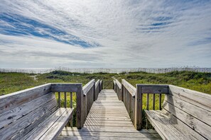 Une promenade en bois menant à une plage, avec une zone herbeuse et un ciel nuageux.