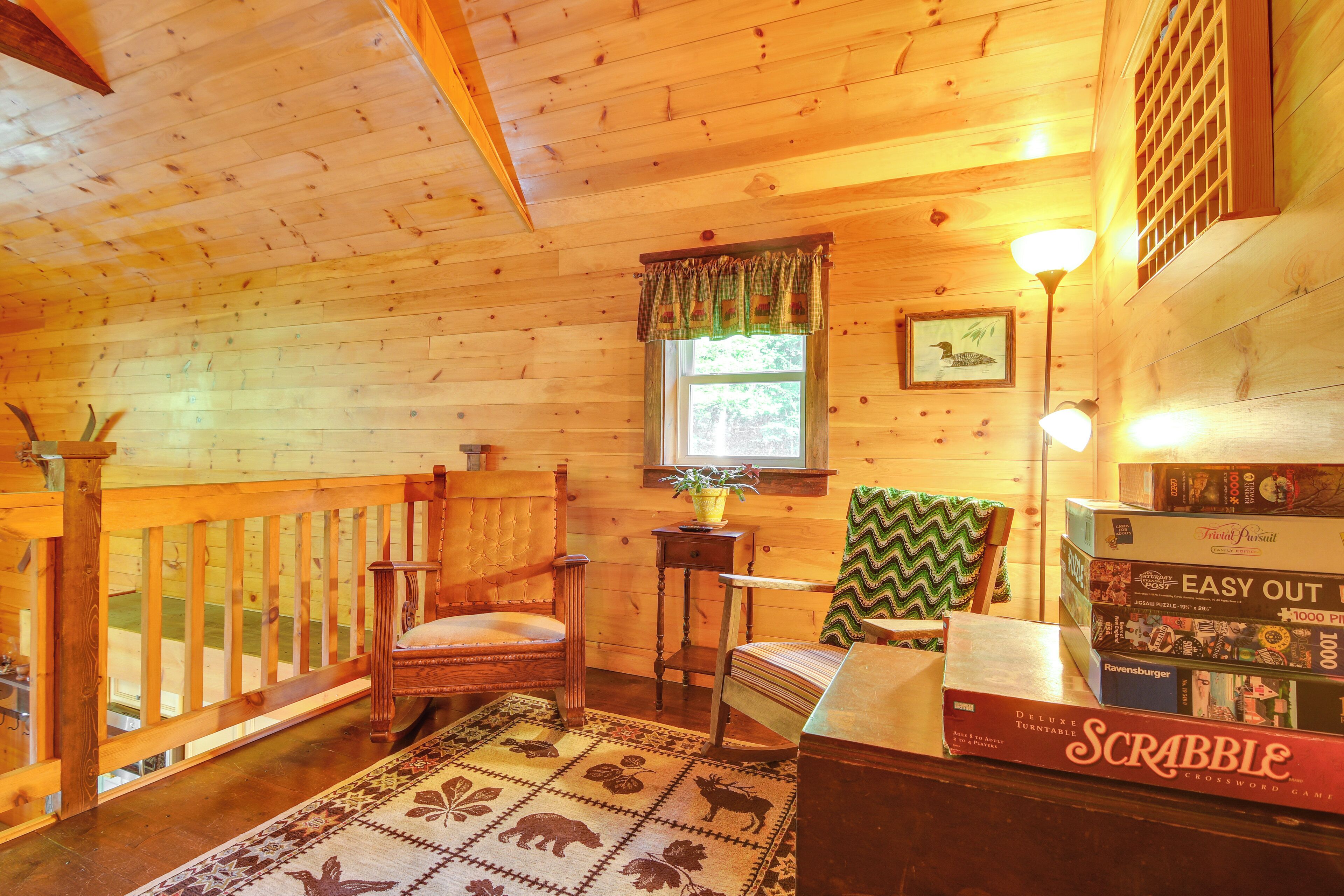 A cozy cabin interior with wooden walls, a window with curtains, a fireplace, and a Scrabble game on the table.