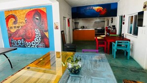 Un salon moderne avec une grande table basse en bois, un coin repas avec des chaises colorées et une cuisine en arrière-plan.