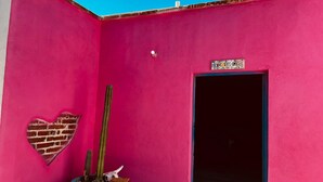 Un mur rose orné d’un cactus dans un pot bleu, d’une découpe en forme de cœur et d’une porte sur laquelle est accrochée une enseigne.