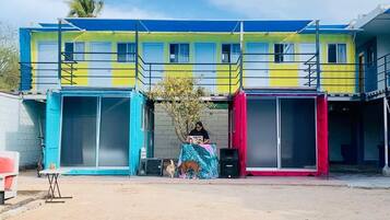 A multi-story building with a blue and yellow facade, a covered outdoor seating area, and a small tree in front.