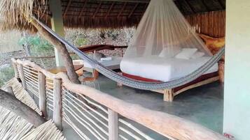 A hammock bed with a mosquito net, wooden railings, and a thatched roof structure.