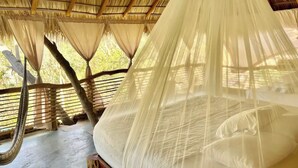Una cama con dosel, piso de madera y estructura de techo de paja.