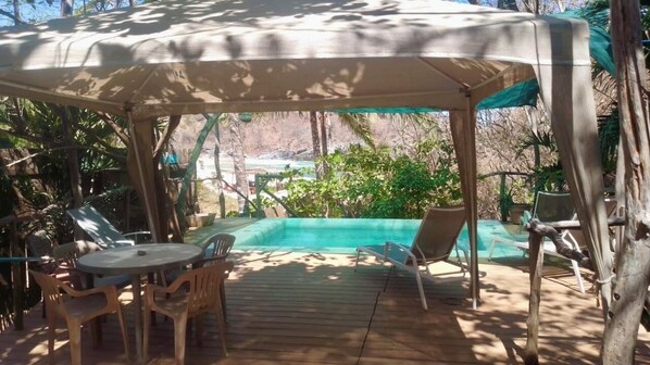 A covered outdoor area with a pool, lounge chairs, and a table.