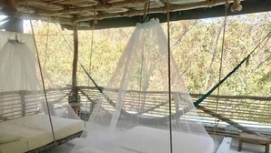 Ein Zimmer mit einem Bett unter einem Moskitonetz, einem weiteren Bett mit Baldachin und Blick auf Bäume.