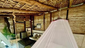 Ein Zimmer mit einem Bett, das mit einem Moskitonetz verhängt ist, einer Couch, einem kleinen Tisch und einer Pflanze.