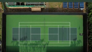 Luchtbeeld van een tennisbaan met omliggend groen en een gebouw met zonnepanelen.