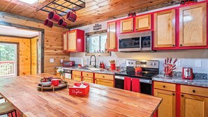 A modern kitchen with wooden cabinets, stainless steel appliances, and a wooden dining table. - Cozy Family Cabin in charming Smoky Mountain- Pets allowed  (Cosby)