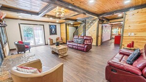 A spacious living area with wooden floors, a red leather sofa, a beige armchair, and a wooden coffee table. A staircase leads to another room. - Cozy Family Cabin in charming Smoky Mountain- Pets allowed  (Cosby)