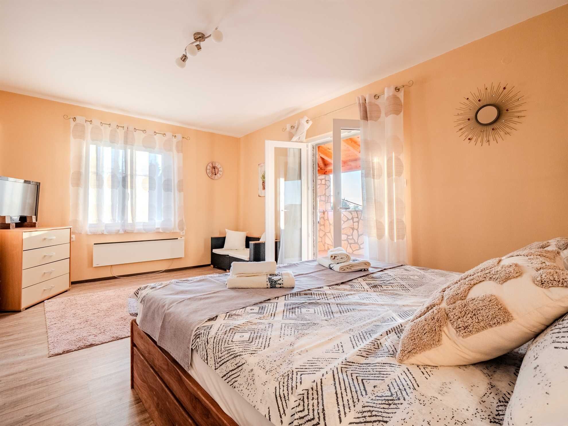 Une chambre à coucher avec un lit, une commode, un téléviseur et une fenêtre avec des rideaux.