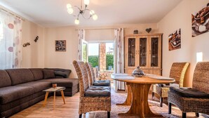 A cozy living room with a sofa, wicker chairs, a wooden dining table, and a chandelier. - Villa Badi with private pool (Malinska (Krk))