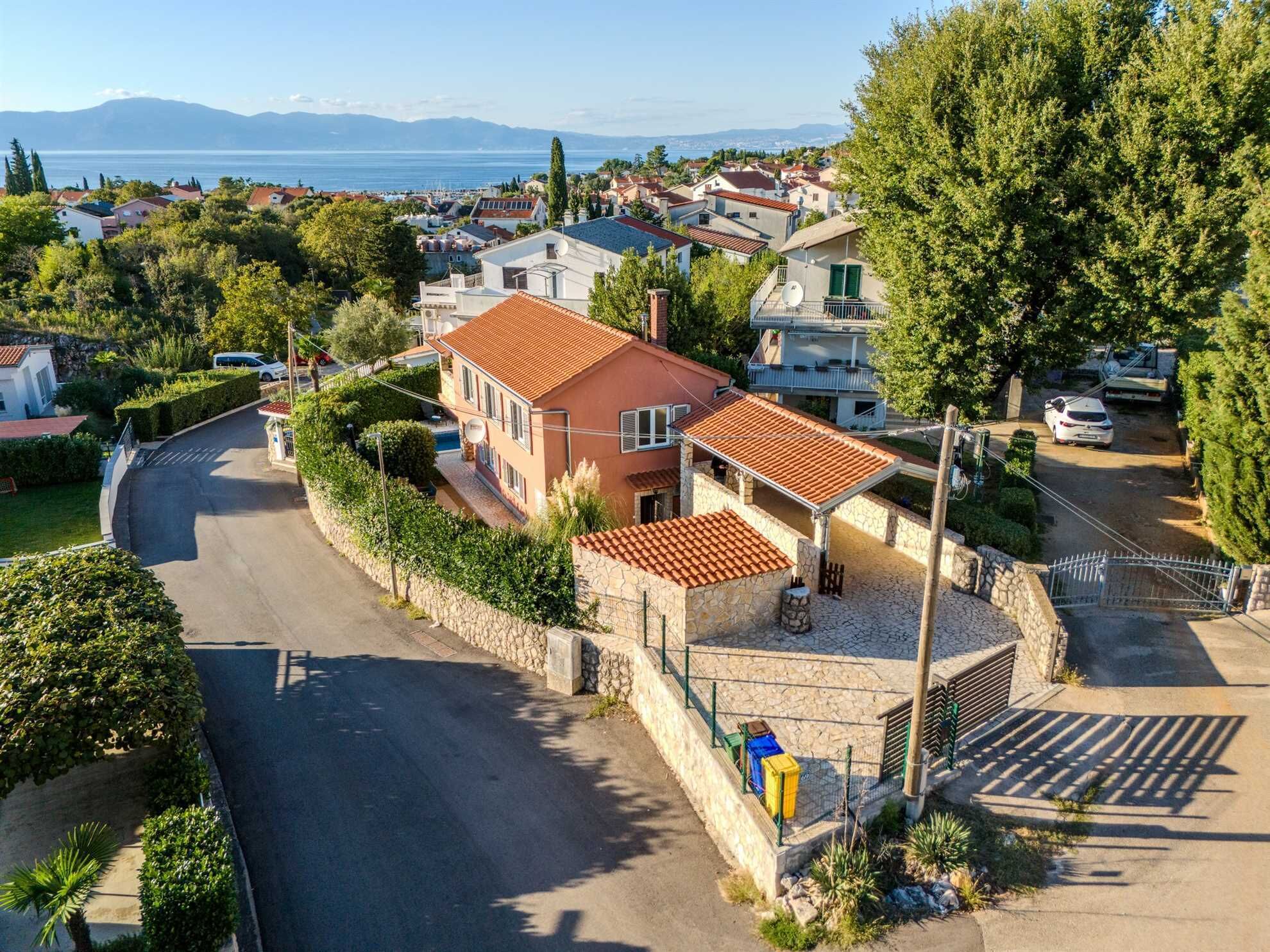 A residential property with a curved driveway, stone walls, and a view of the sea.