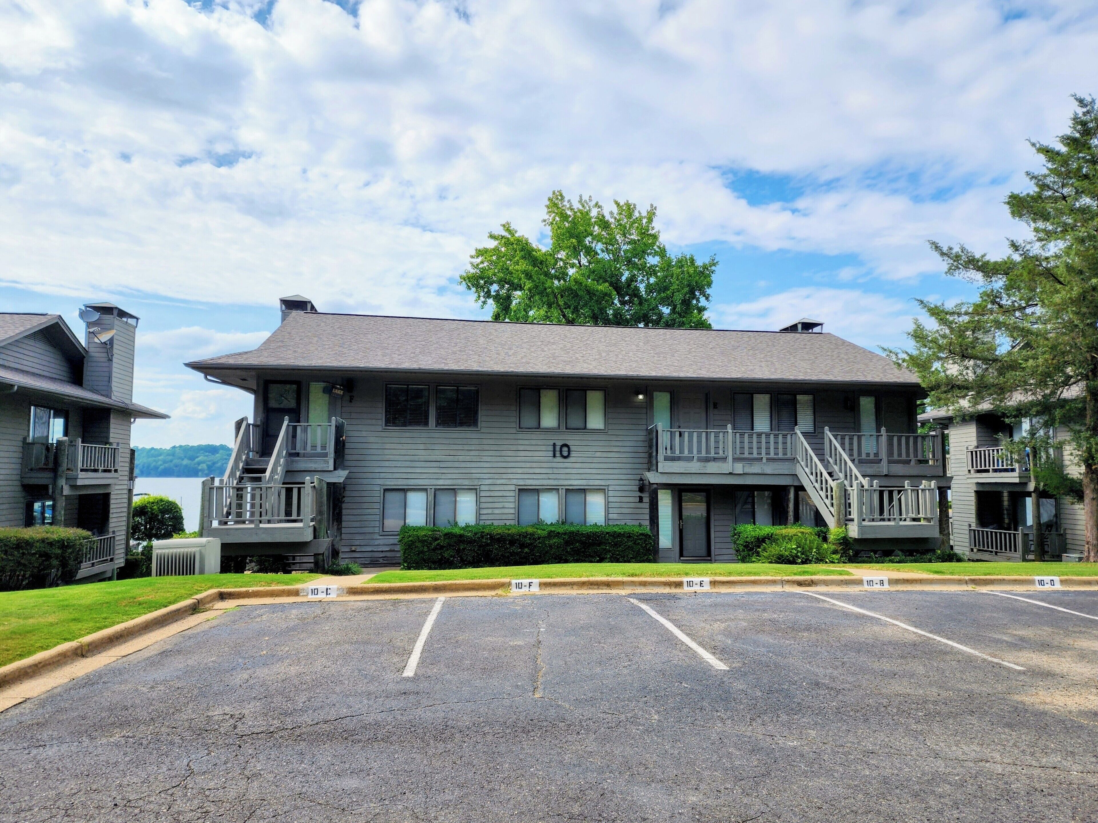 A two-story building with a balcony, a parking lot in front, and a lake in the background.