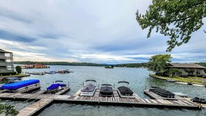 A dock with several boats, a wooden pier, and a view of a lake with buildings in the background. - Farr Shores Cozy Retreat (Hot Springs)