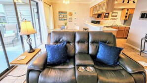 A living room with a leather sofa, a lamp, and a view of the kitchen. - Farr Shores Cozy Retreat (Hot Springs)