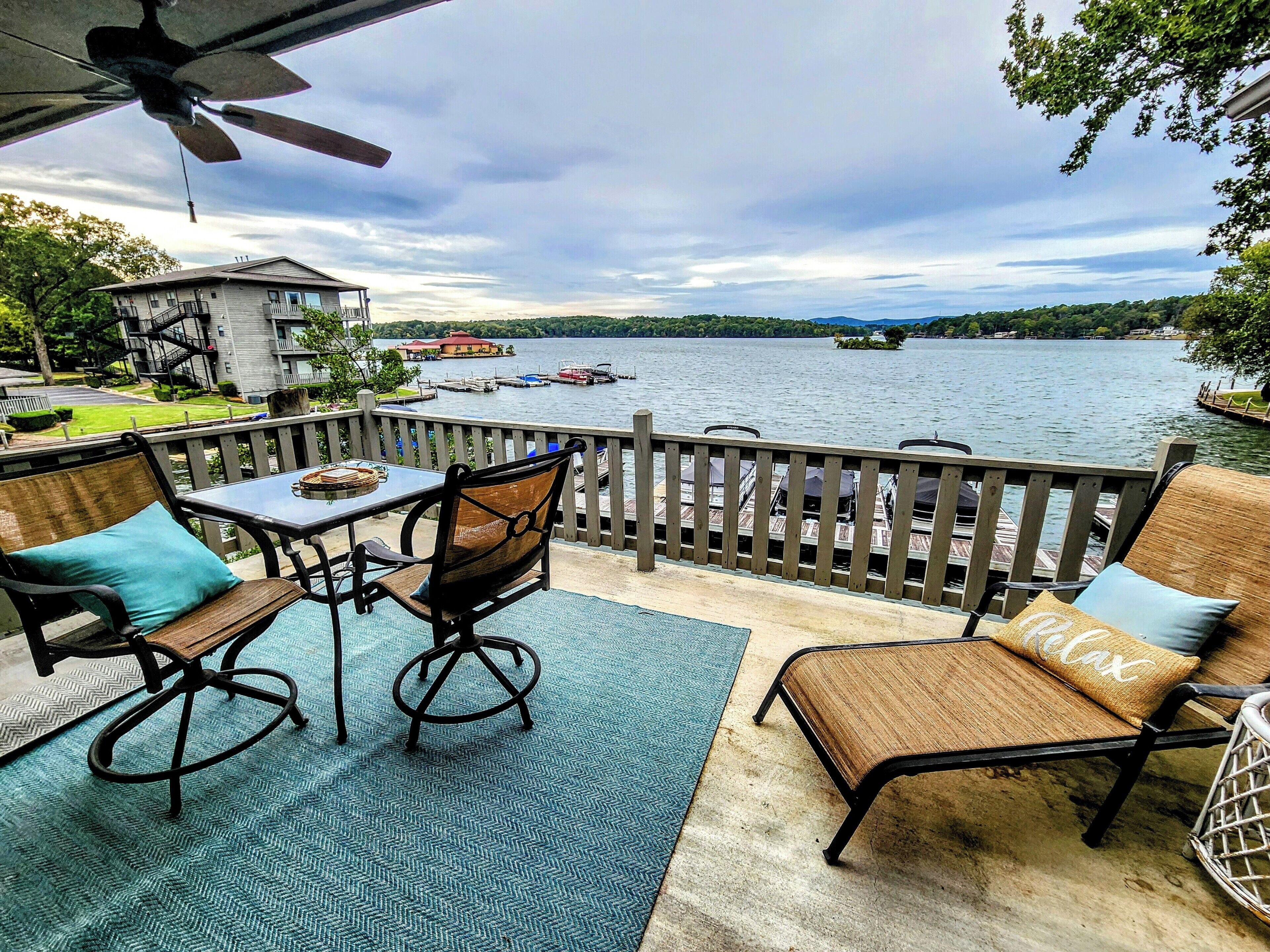A patio with a table and chairs, overlooking a lake with boats and a dock.