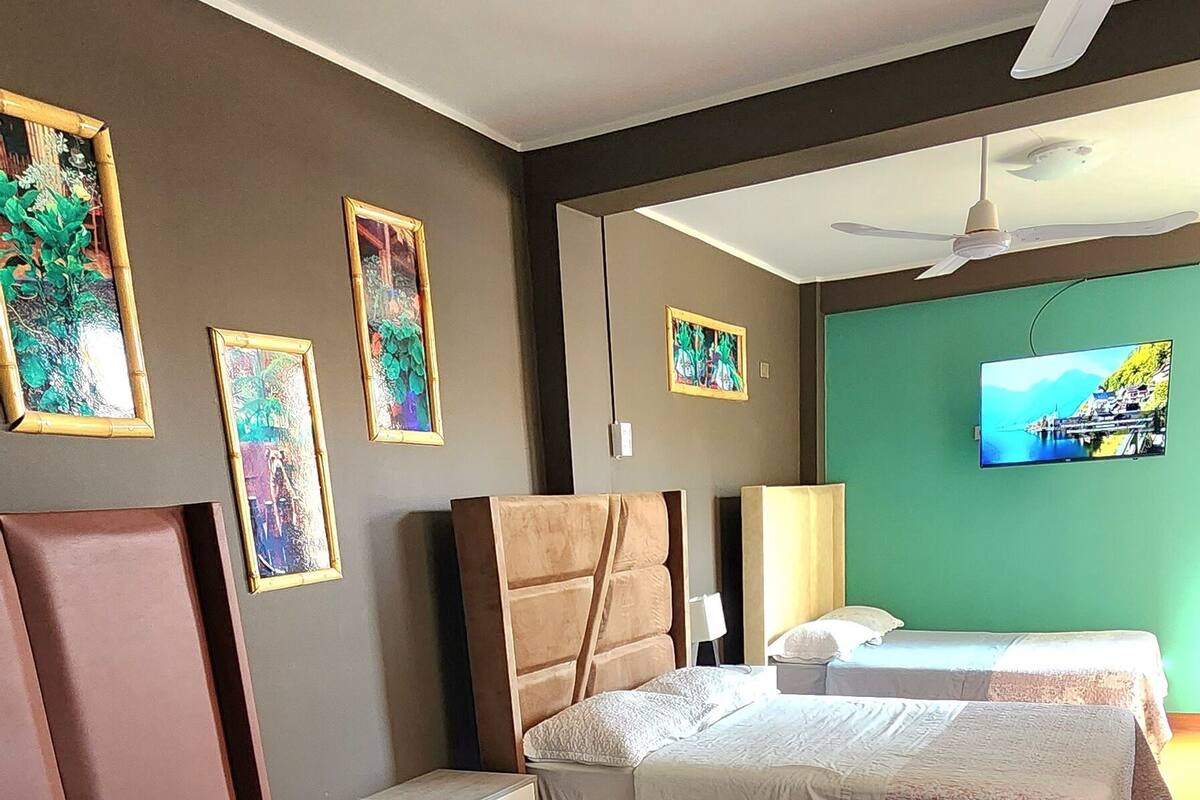 A hotel room with two beds, a ceiling fan, a television, and framed artwork on the wall.