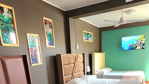 A hotel room with two beds, a ceiling fan, a television, and framed artwork on the wall. - La casa de Bamboo (Ica)