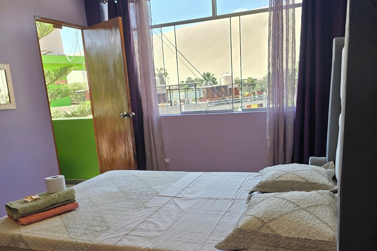 A bedroom with a bed, a ceiling fan, a window with curtains, and a view of the outside.